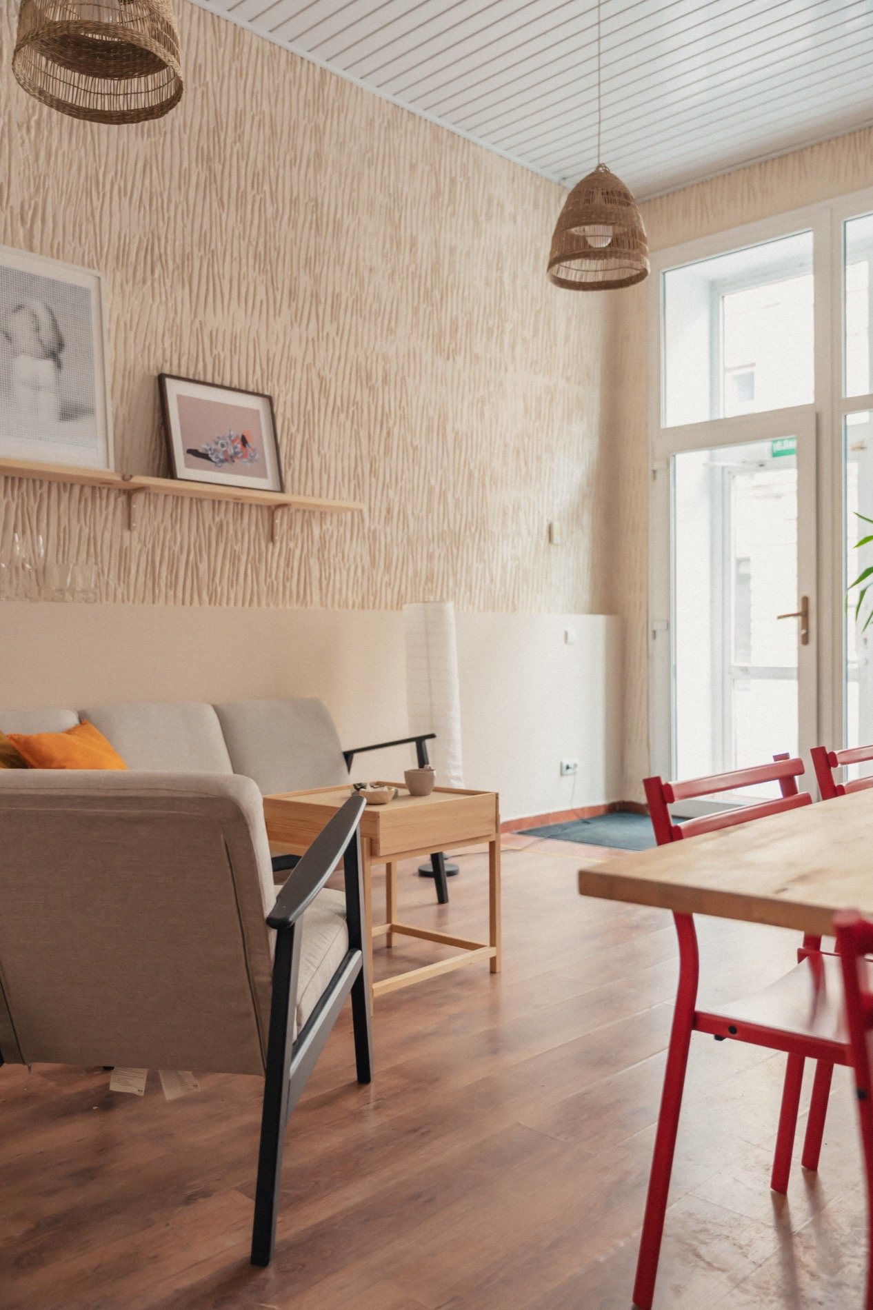 Studijos poilsio kampas su sofa, tekstūrine siena, pakabinamais šviestuvais ir raudonomis kėdėmis